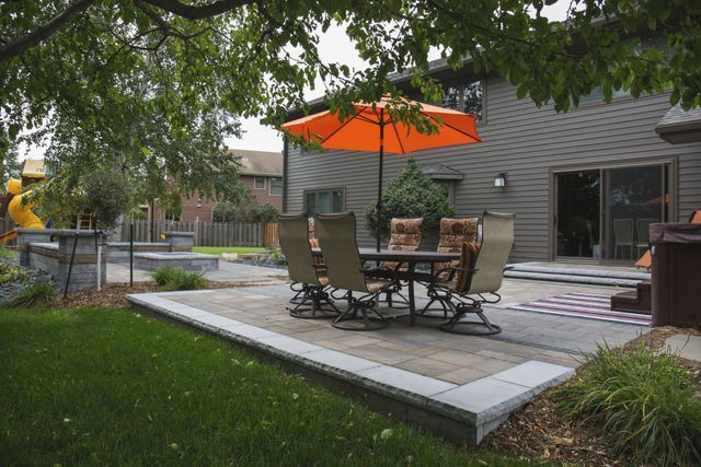 A patio with a table and chairs and an orange umbrella.