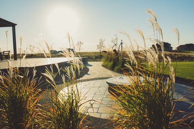 A patio with a gazebo in the background and tall grass in the foreground.