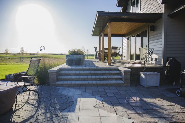 A patio with stairs leading up to a porch and a house in the background.