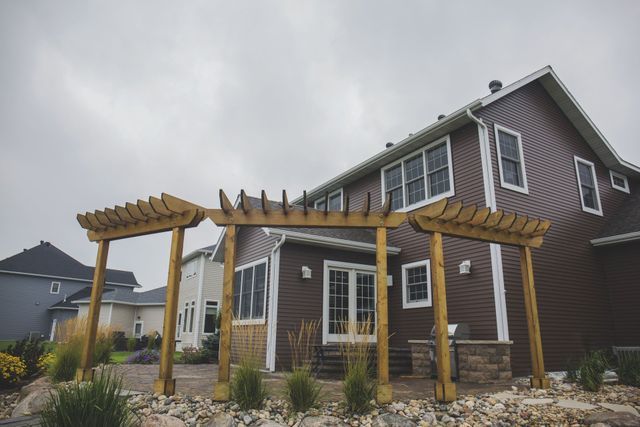 A house with a pergola in front of it on a cloudy day.