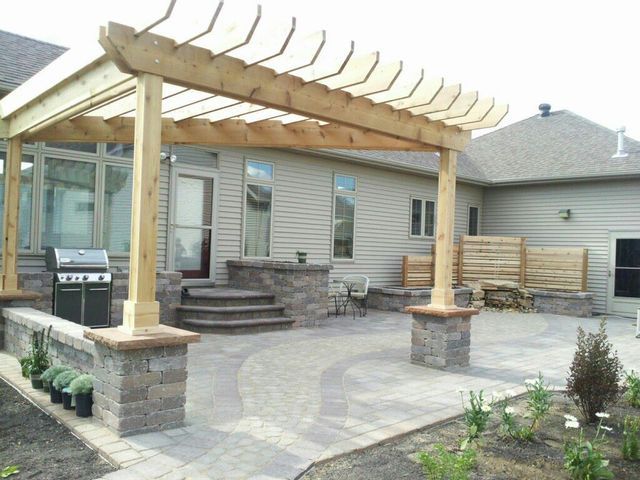 A patio with a wooden pergola and a grill