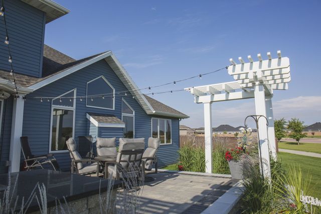A blue house with a white pergola and a patio with a table and chairs.