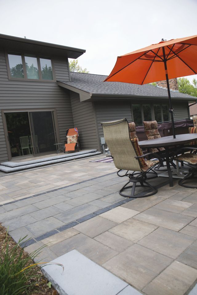 A patio with a table and chairs and an orange umbrella in front of a house.