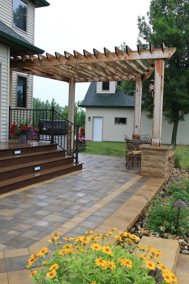 A patio with a pergola and flowers in front of a house