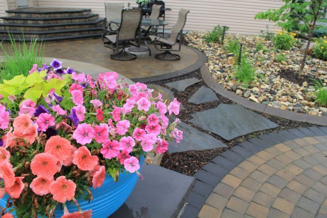 A blue pot filled with pink and purple flowers is in the middle of a patio.