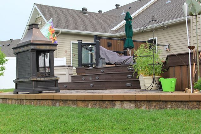 A deck with a fireplace and umbrellas in front of a house.