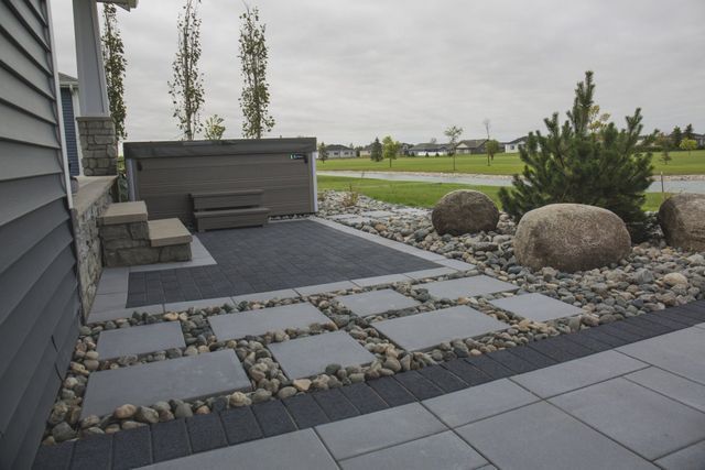 A patio with a hot tub and rocks in front of a house.