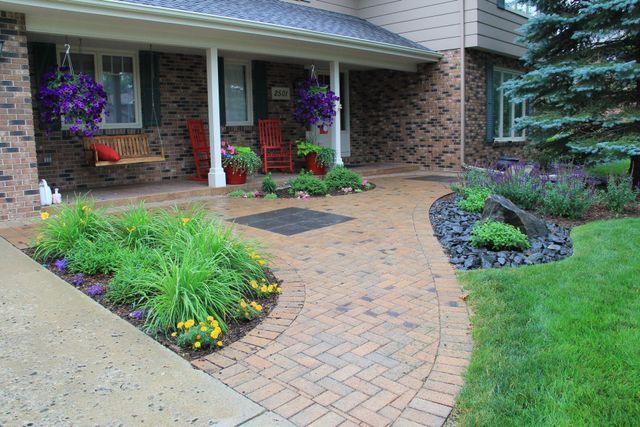 A brick walkway leading to a porch with a bench and chairs.