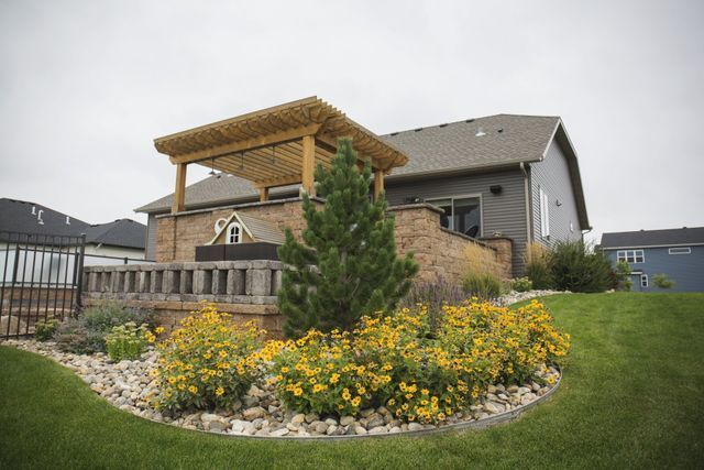 A house with a pergola and flowers in front of it.