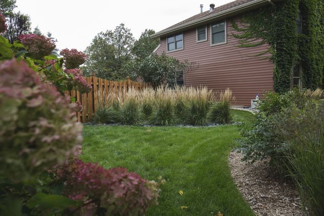 A lush green yard with a fence and flowers in front of a brick house.