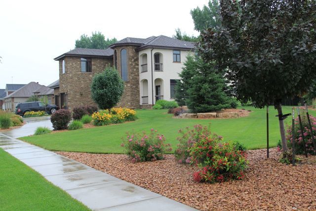 A large house is sitting on top of a lush green lawn next to a sidewalk.
