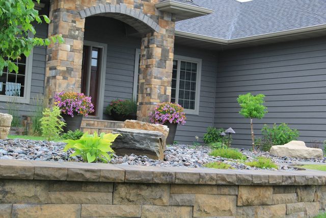 A house with a stone wall and flowers in front of it.