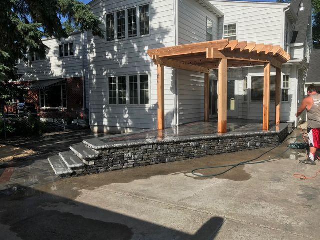 A man is standing in front of a house with a pergola.