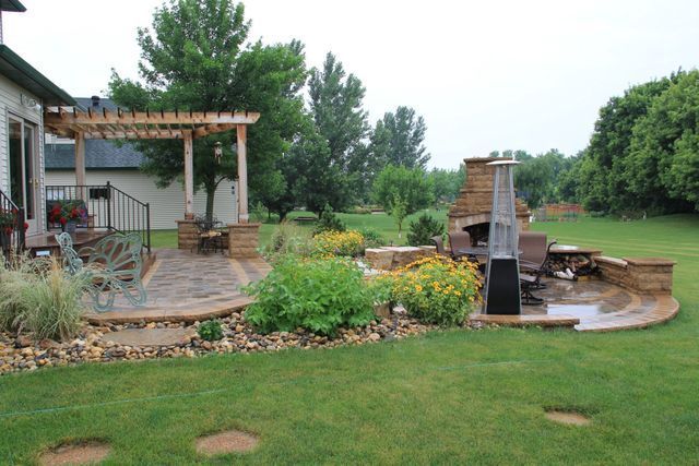A patio with a pergola and a fireplace in the backyard of a house.