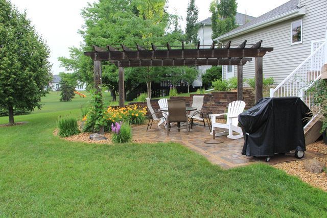 A patio with a pergola and a grill in the backyard of a house.