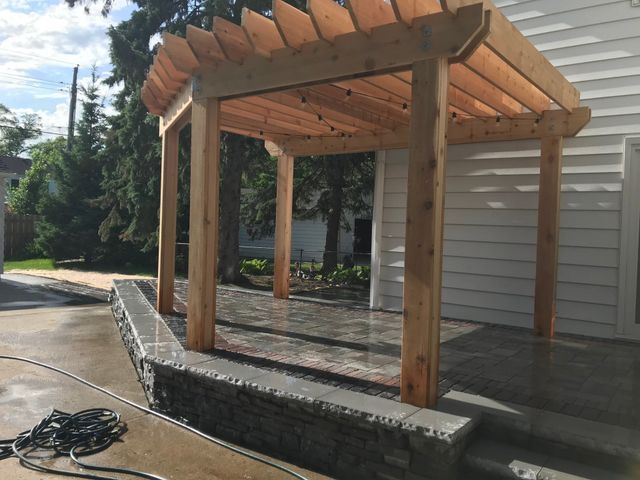 A wooden pergola is sitting in front of a white house.