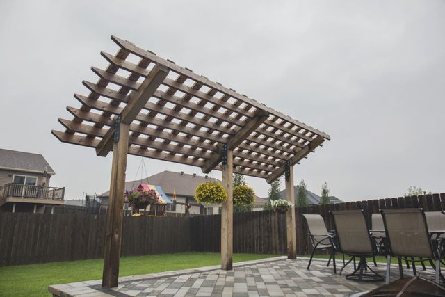 A wooden pergola is sitting on top of a patio next to a table and chairs.