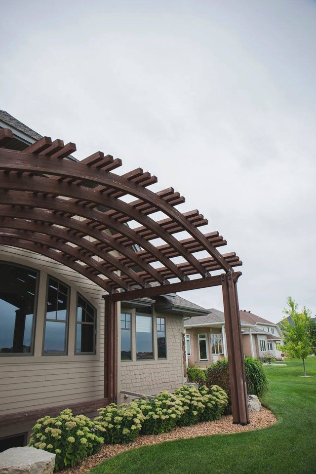 A wooden pergola is in the backyard of a house.