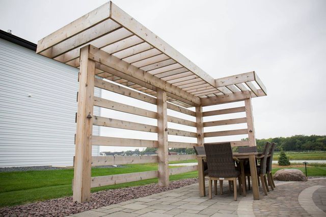 A wooden pergola with a table and chairs underneath it