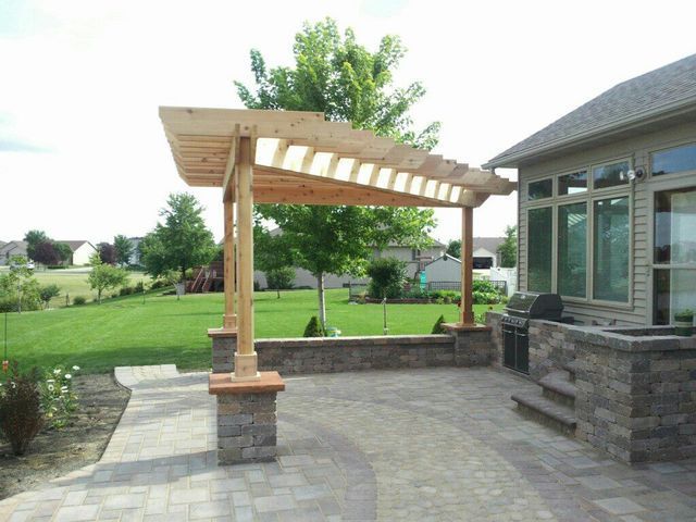 A patio with a pergola and a grill in front of a house