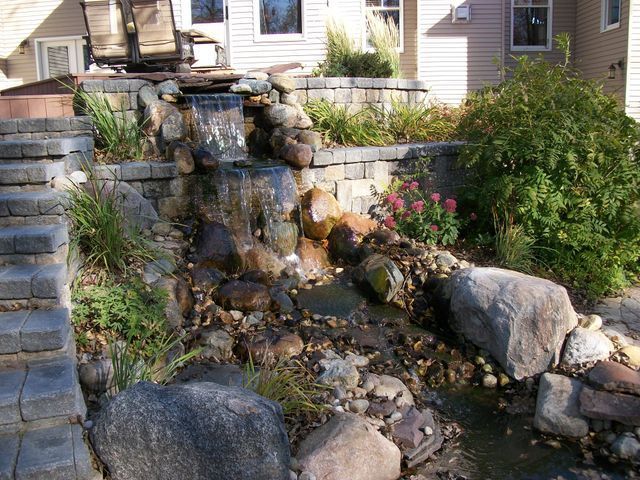 A waterfall is surrounded by rocks and stairs in front of a house