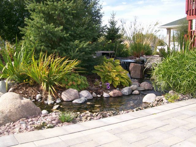 A pond surrounded by rocks and trees with a house in the background