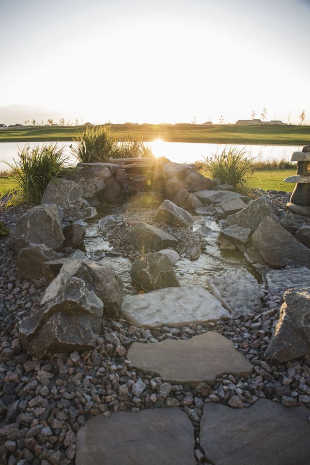 The sun is setting over a pond surrounded by rocks.