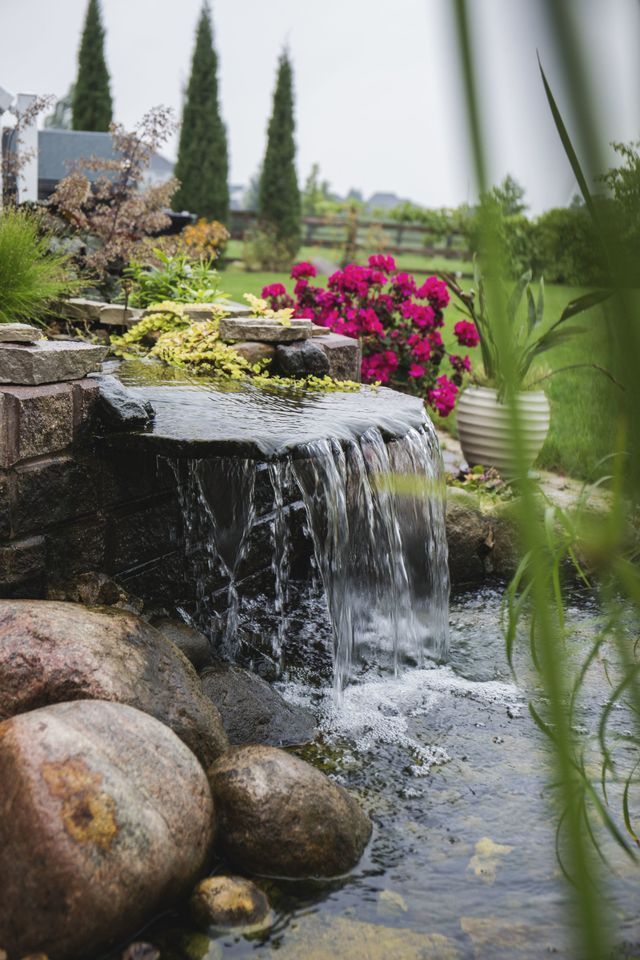A waterfall is surrounded by rocks and flowers in a garden.