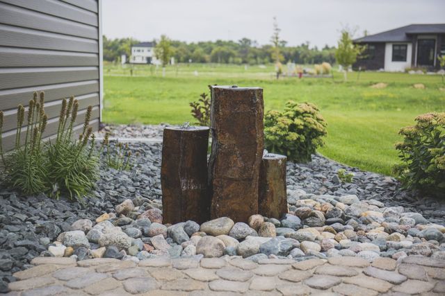 A water fountain made of logs and rocks in front of a house.