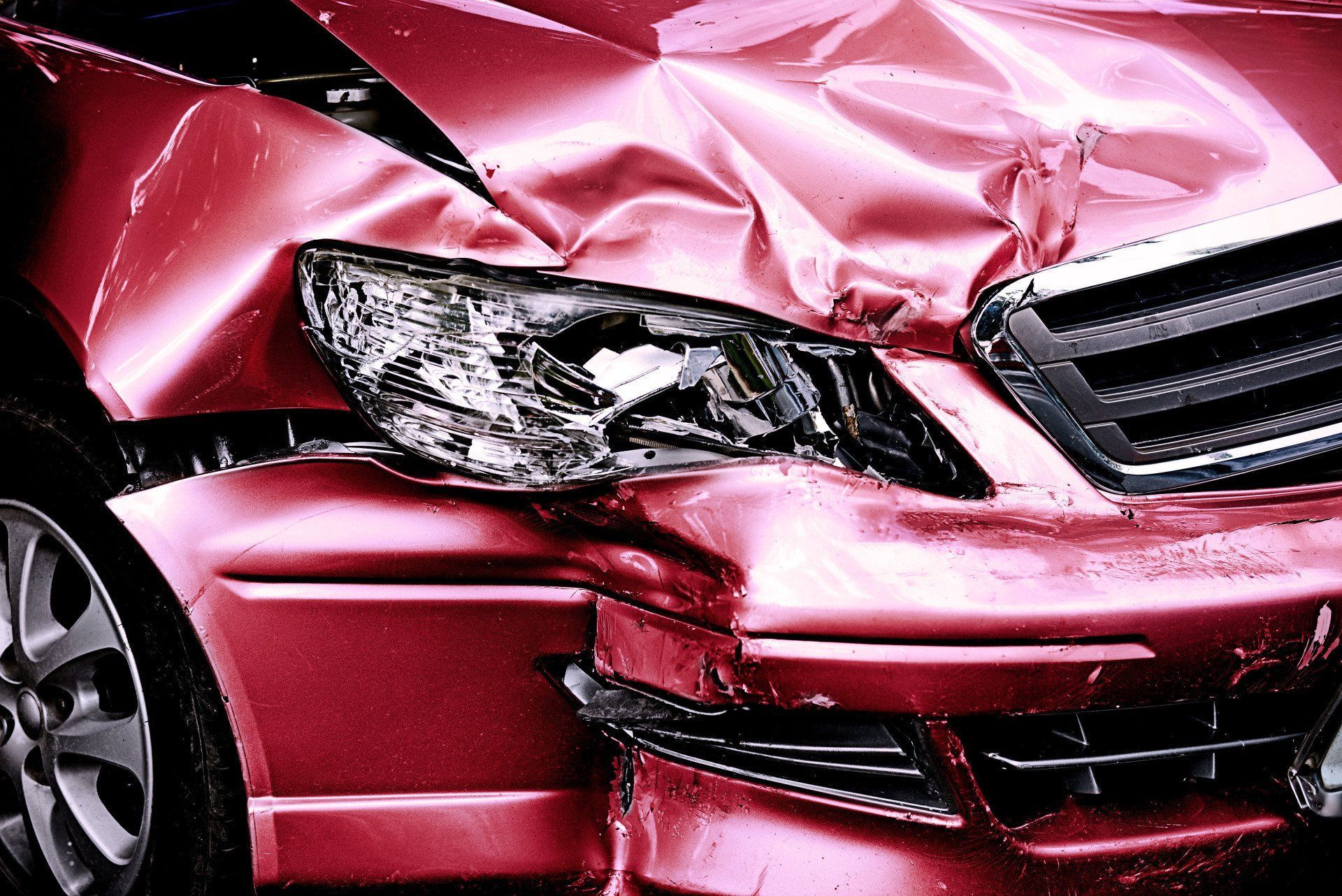 Front-end of a red car with severe crash damage and a crushed hood.