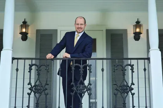 Kevin E. Broussard, Attorney at Law standing on a balcony with black wrought-iron railings in front of white shutters.
