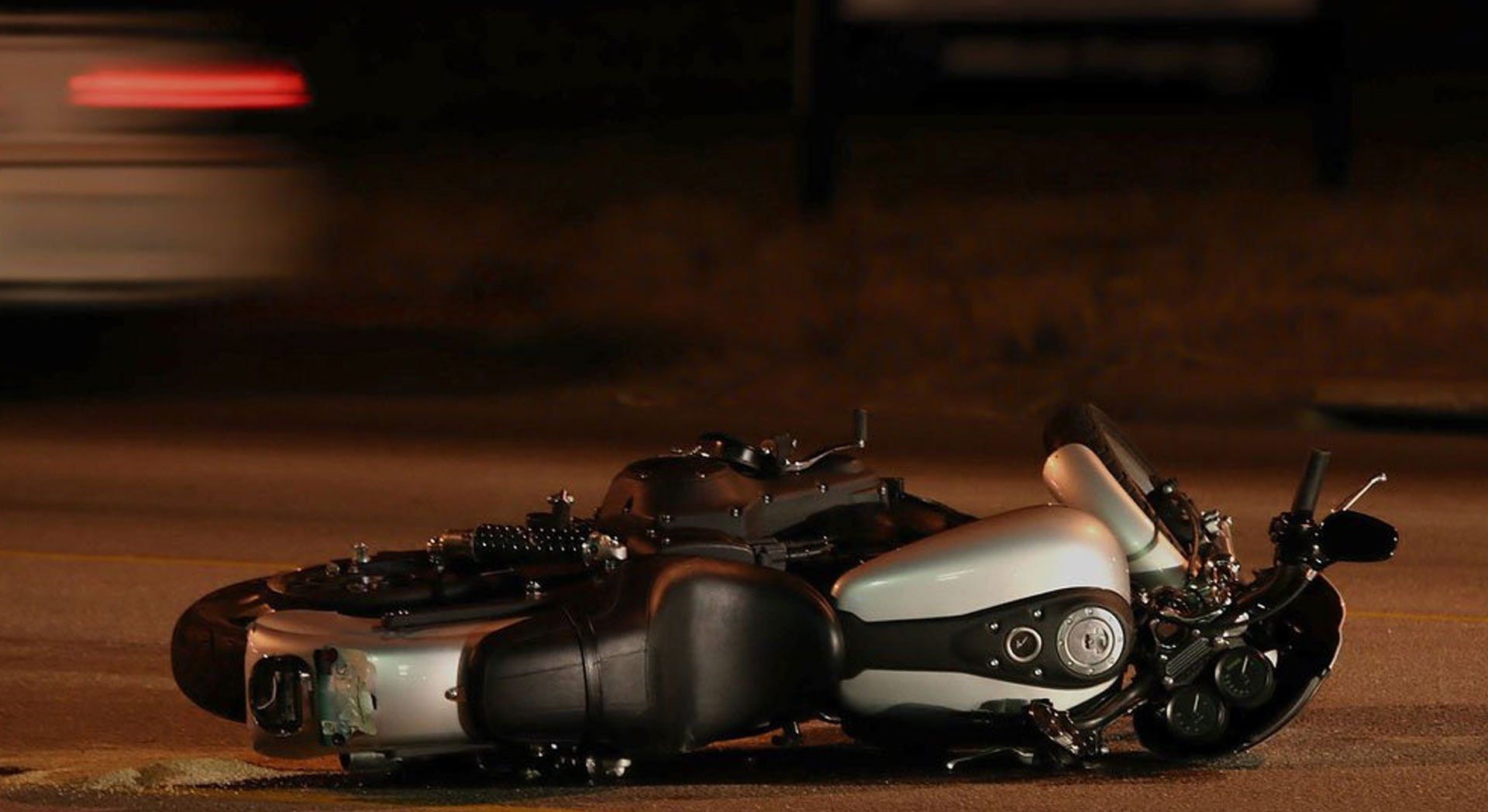 A black-and-white toy motorcycle lies on its side on a dimly lit road at night.