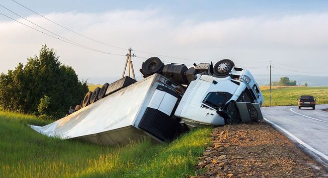 Overturned white truck in a roadside ditch beside a rural road at sunset