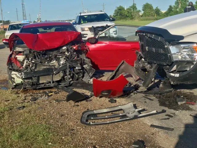 Severe head-on car crash with a red car and a white truck, both heavily damaged on a roadside