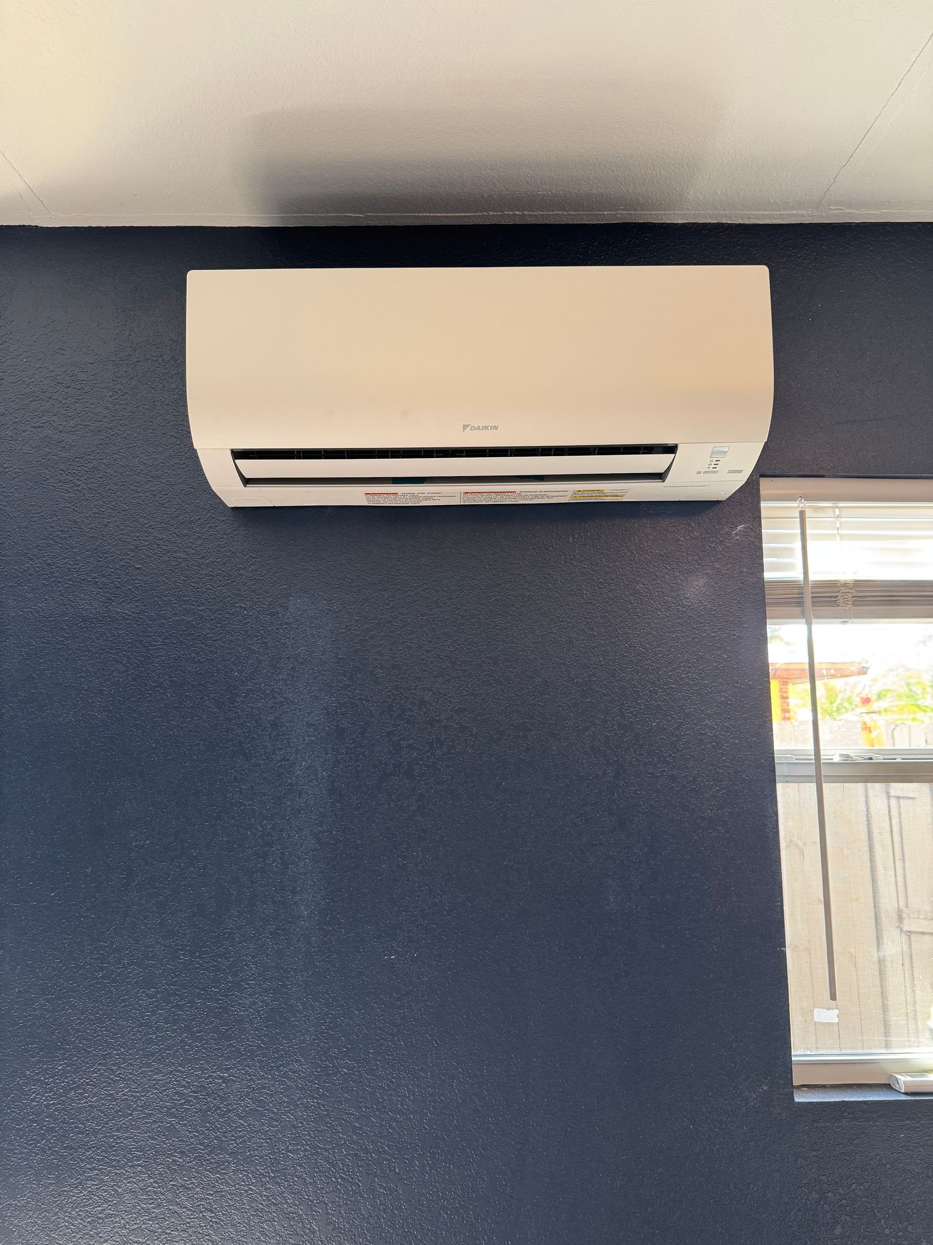 White wall-mounted air conditioner on a blue textured wall beside a window.