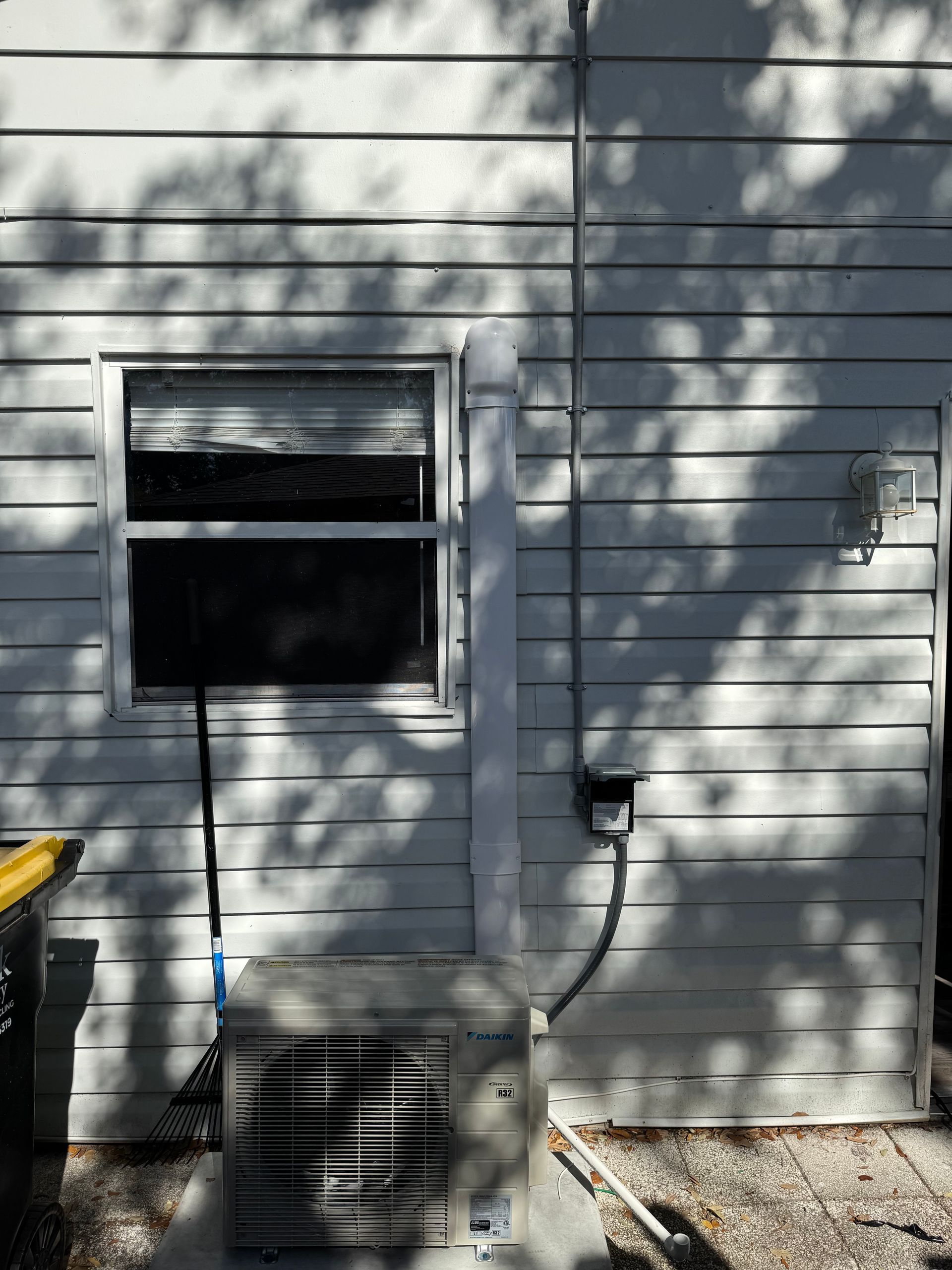 White house siding with a small window, outdoor AC unit, and tree shadows on the wall.