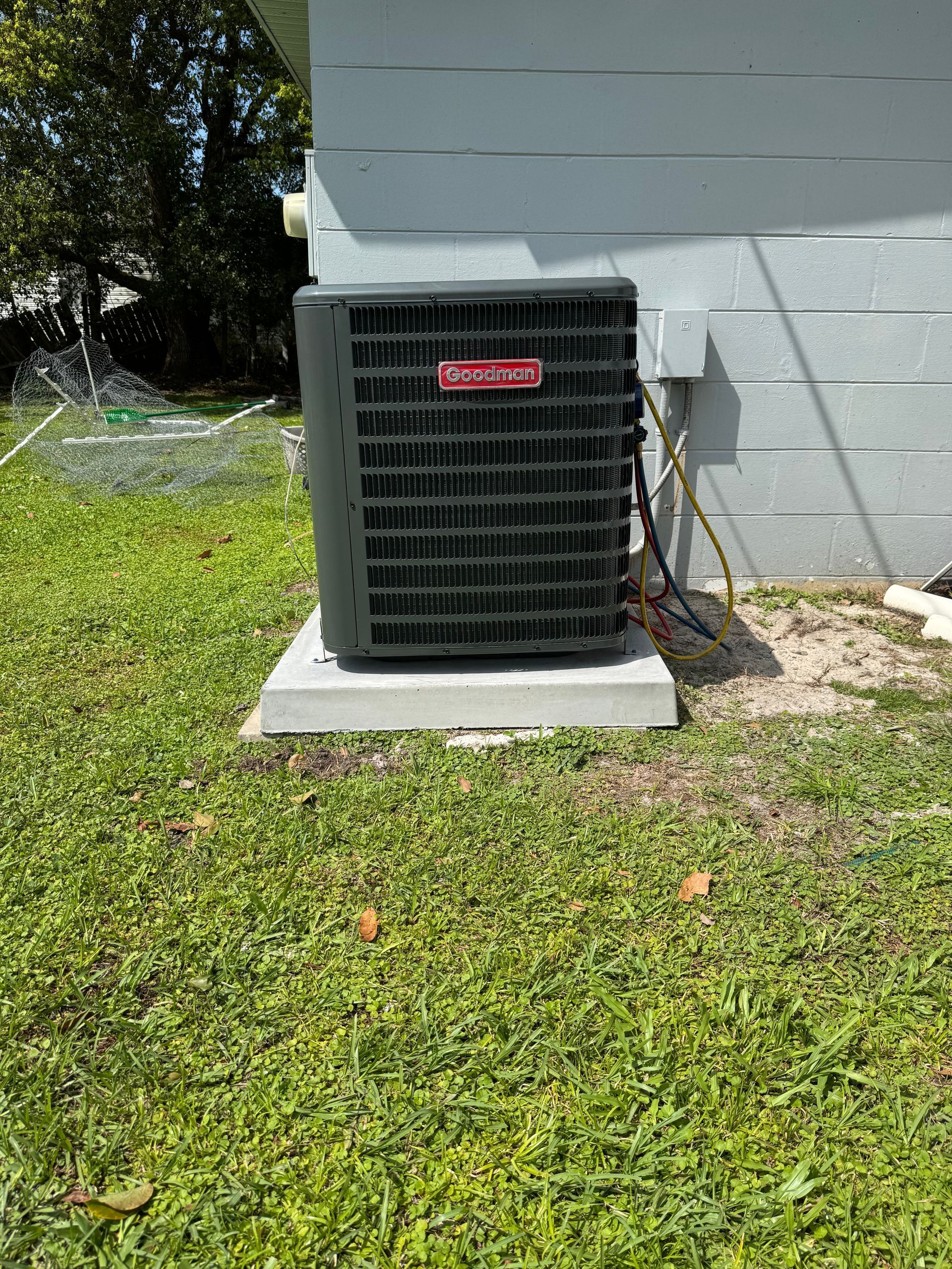 Outdoor air conditioner unit beside a house wall on a grassy lawn.