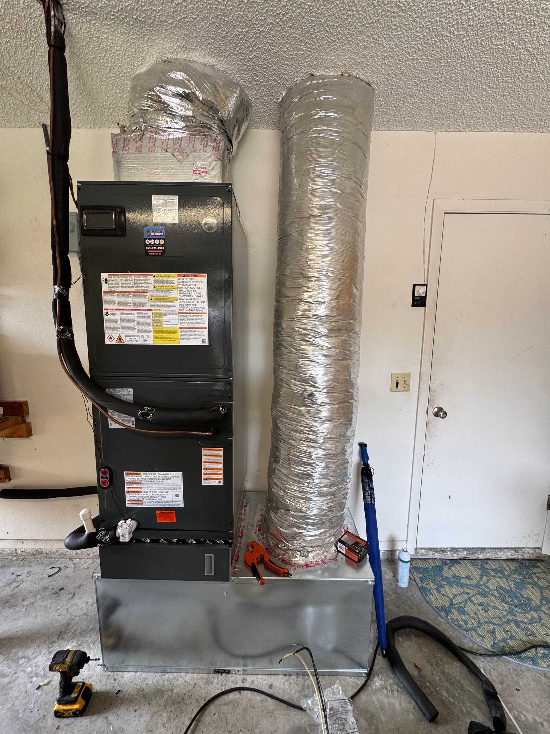 HVAC unit and silver ductwork in a utility room with tools on the floor