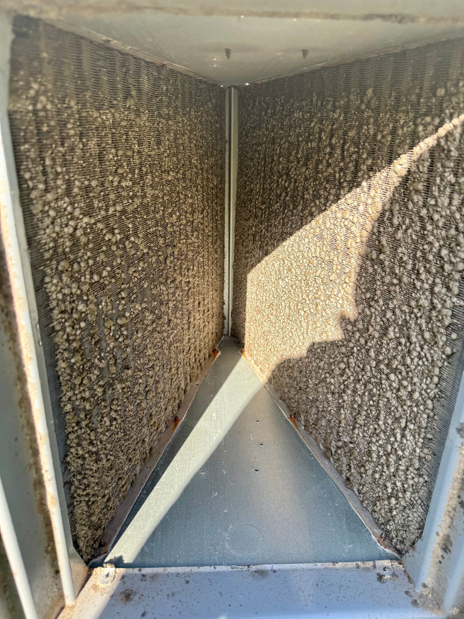 Textured metal interior of a vent or duct, with a triangular shadow and sunlight on one side