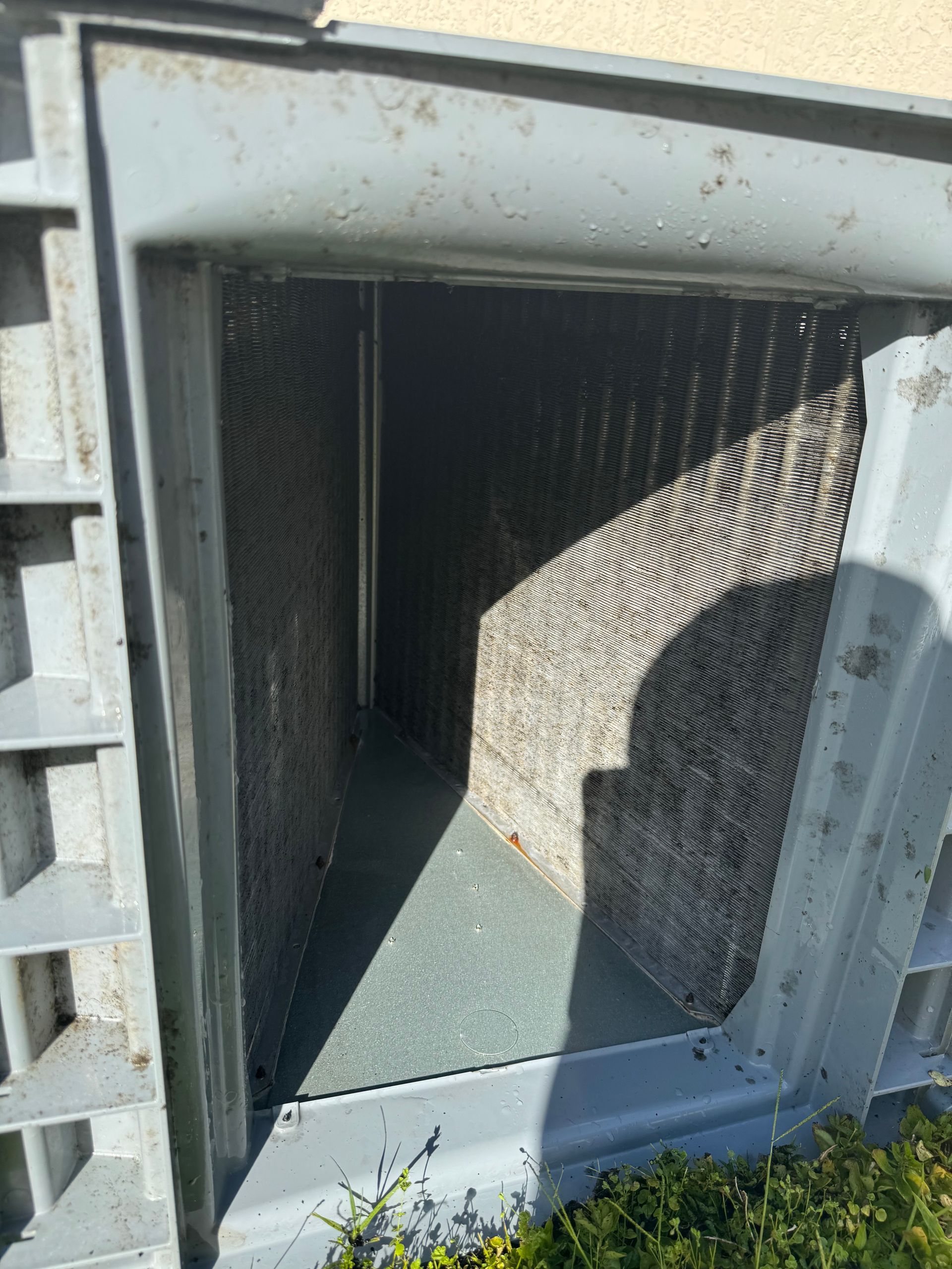 Open HVAC duct with metal frame and dark interior, showing a honeycomb filter and sunlight shadow.