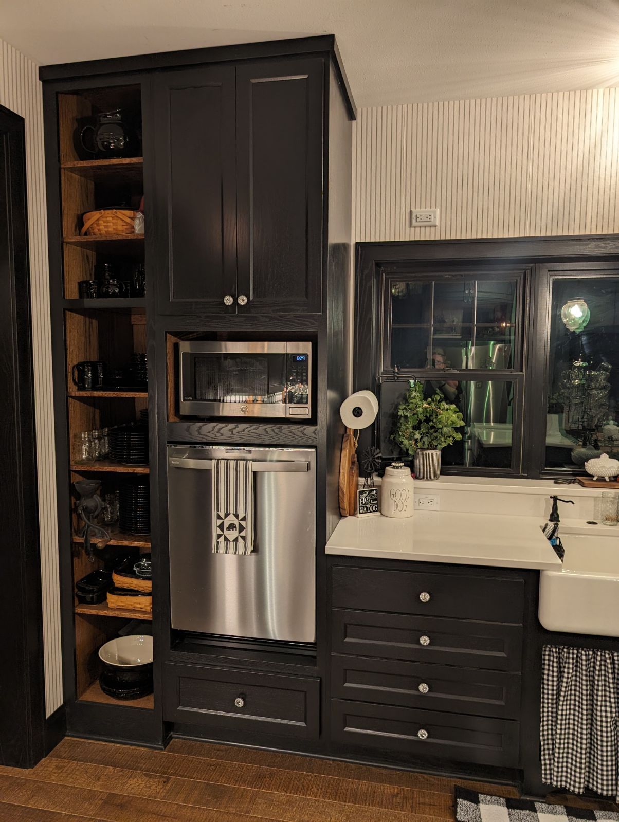 A kitchen with black cabinets, stainless steel refrigerator, a microwave, and a sink