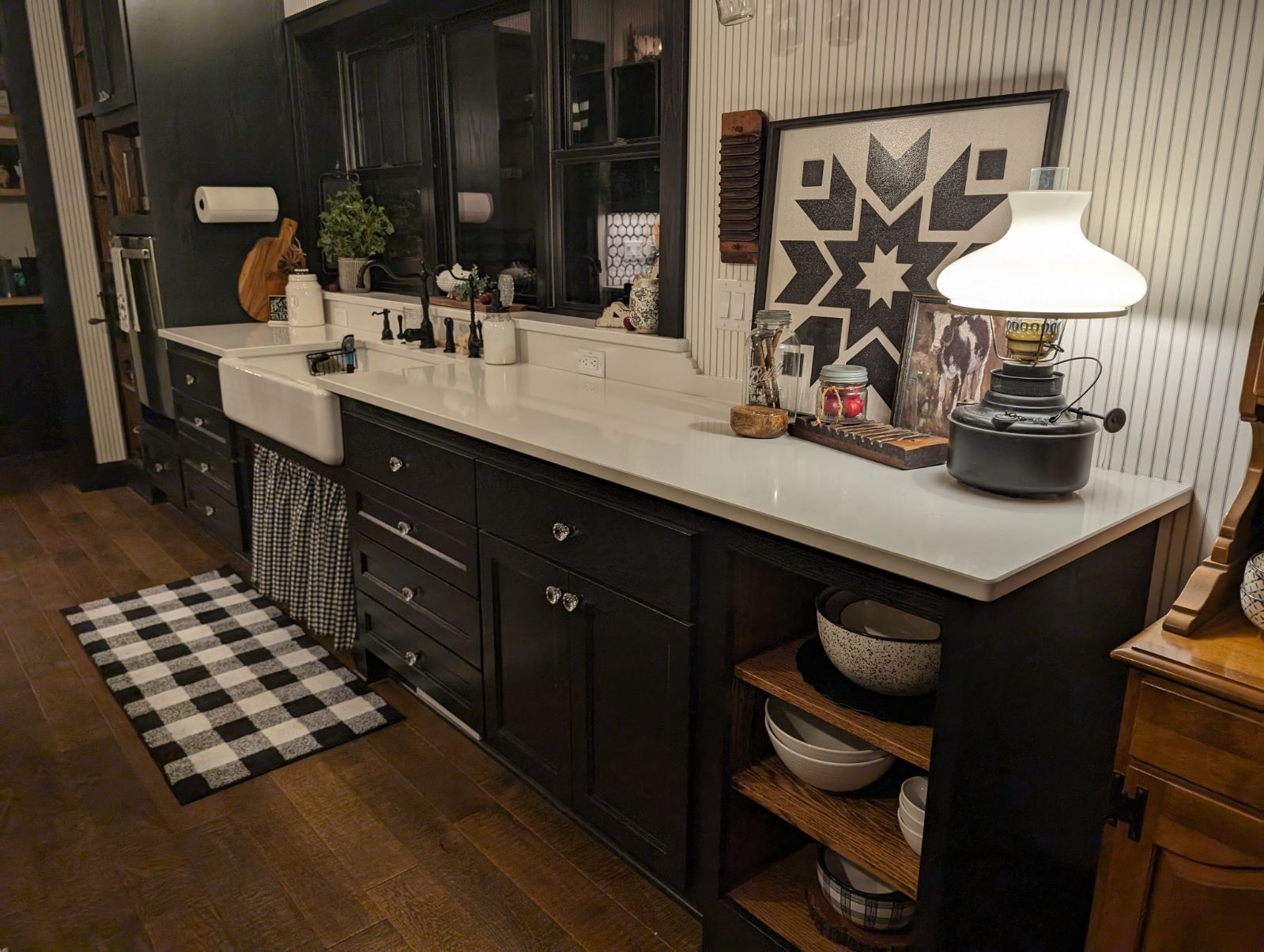 A kitchen with black cabinets, a sink, a lamp, and a plaid rug