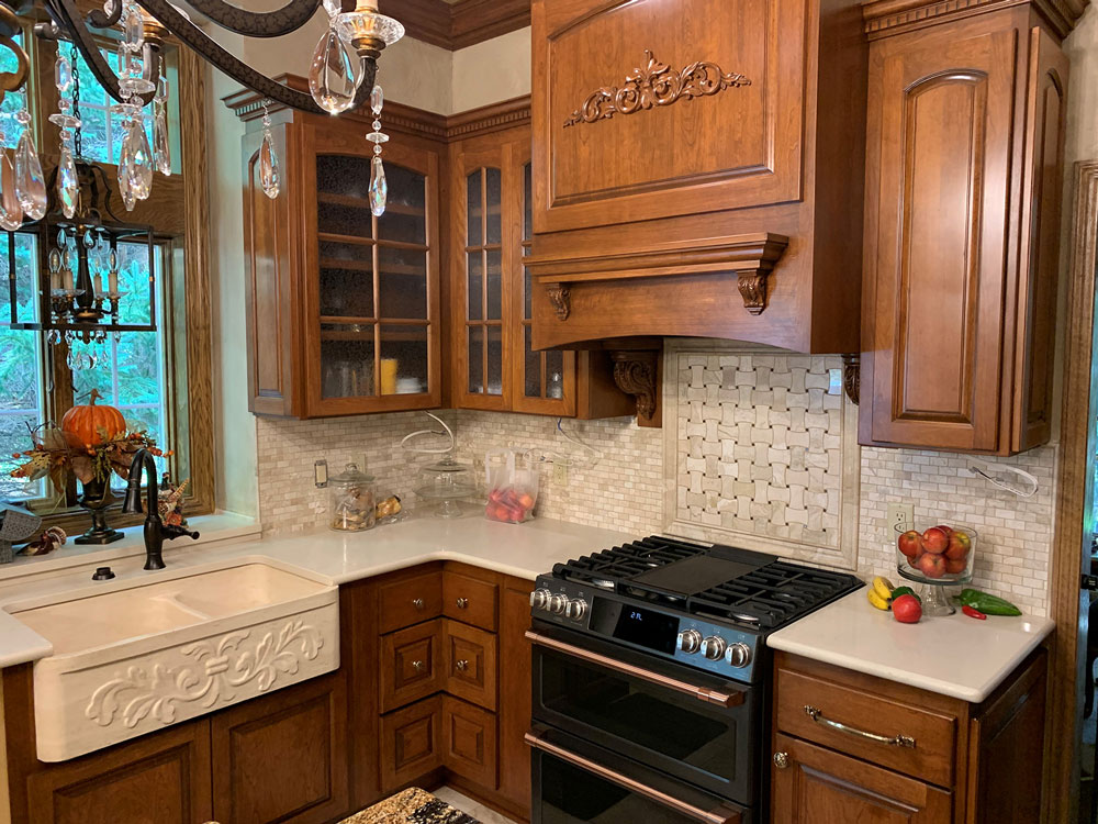 A kitchen with wooden cabinets , a stove , a sink , and a chandelier.