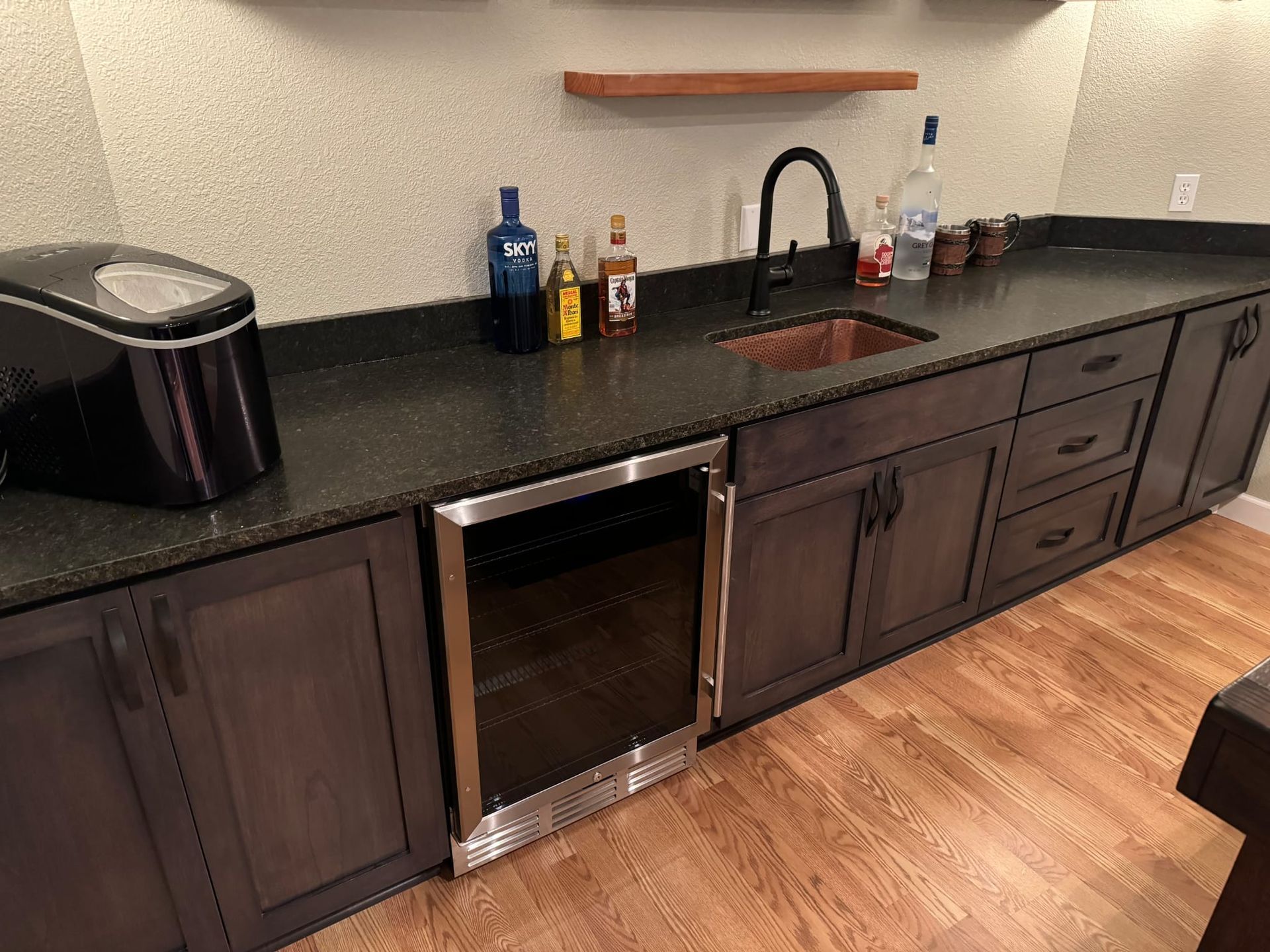 A kitchen with a sink , refrigerator , and bottles on the counter.