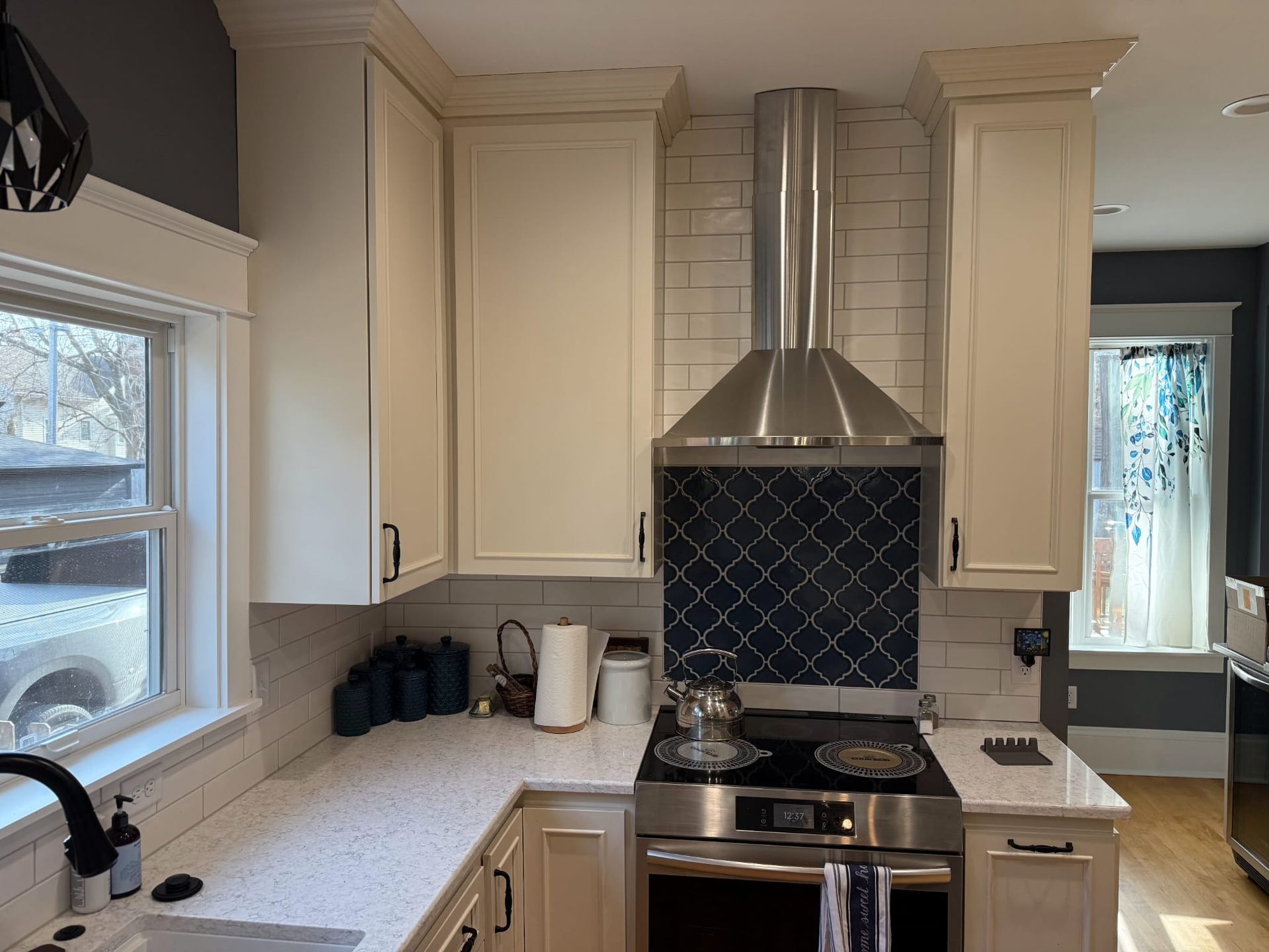 A kitchen with white cabinets , a stove , a sink , and a window.