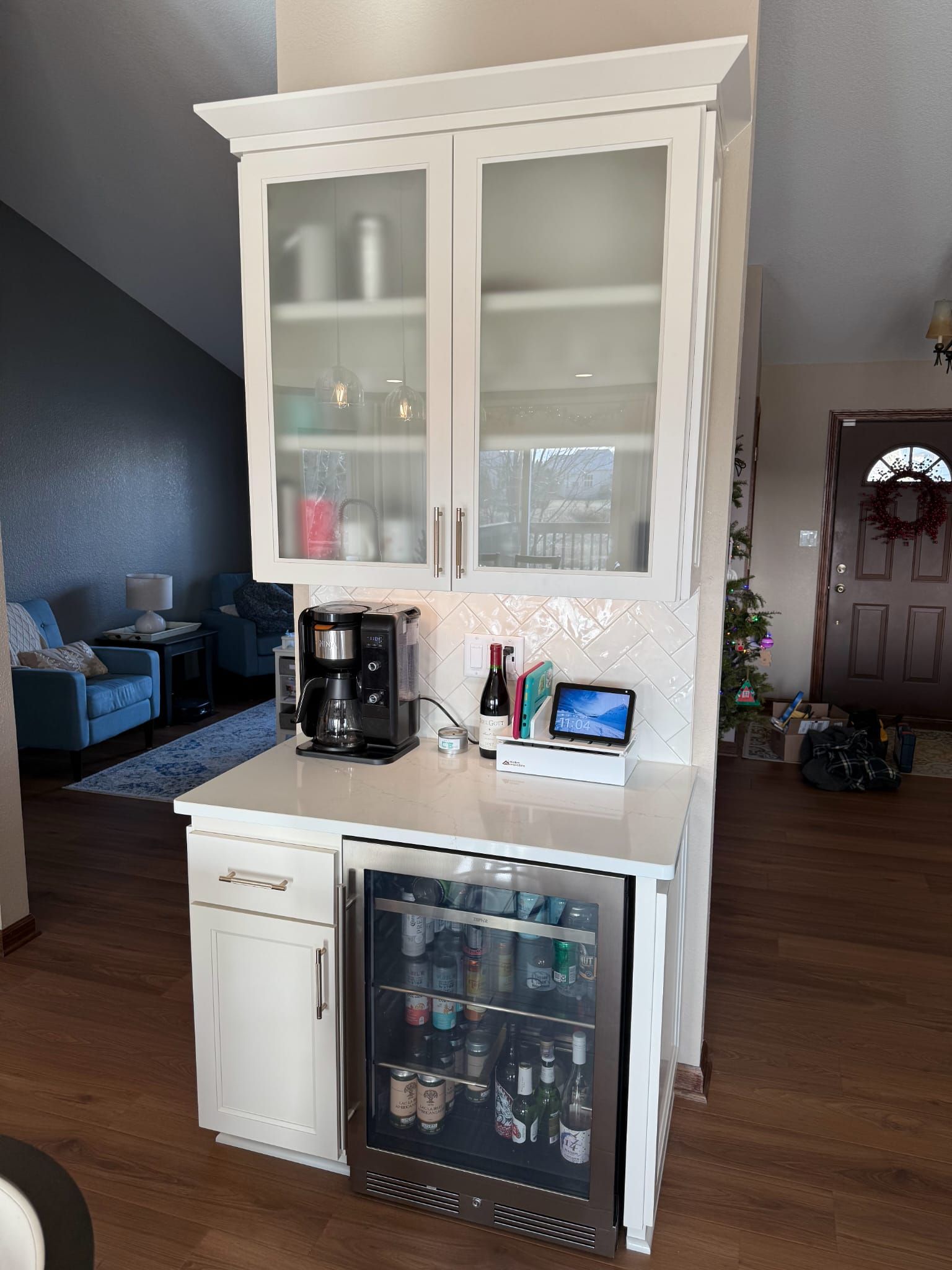 A kitchen with white cabinets , a refrigerator , a coffee maker , and a bar.