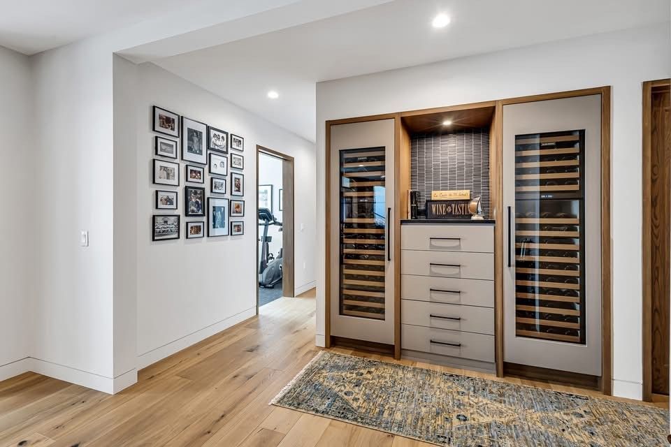 Modern home hallway with a walk-in wine cabinet, hardwood floors, and framed wall art.