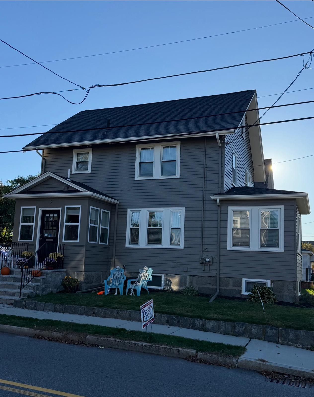 Two-story gray house with white trim and small front porch on a residential street at dusk