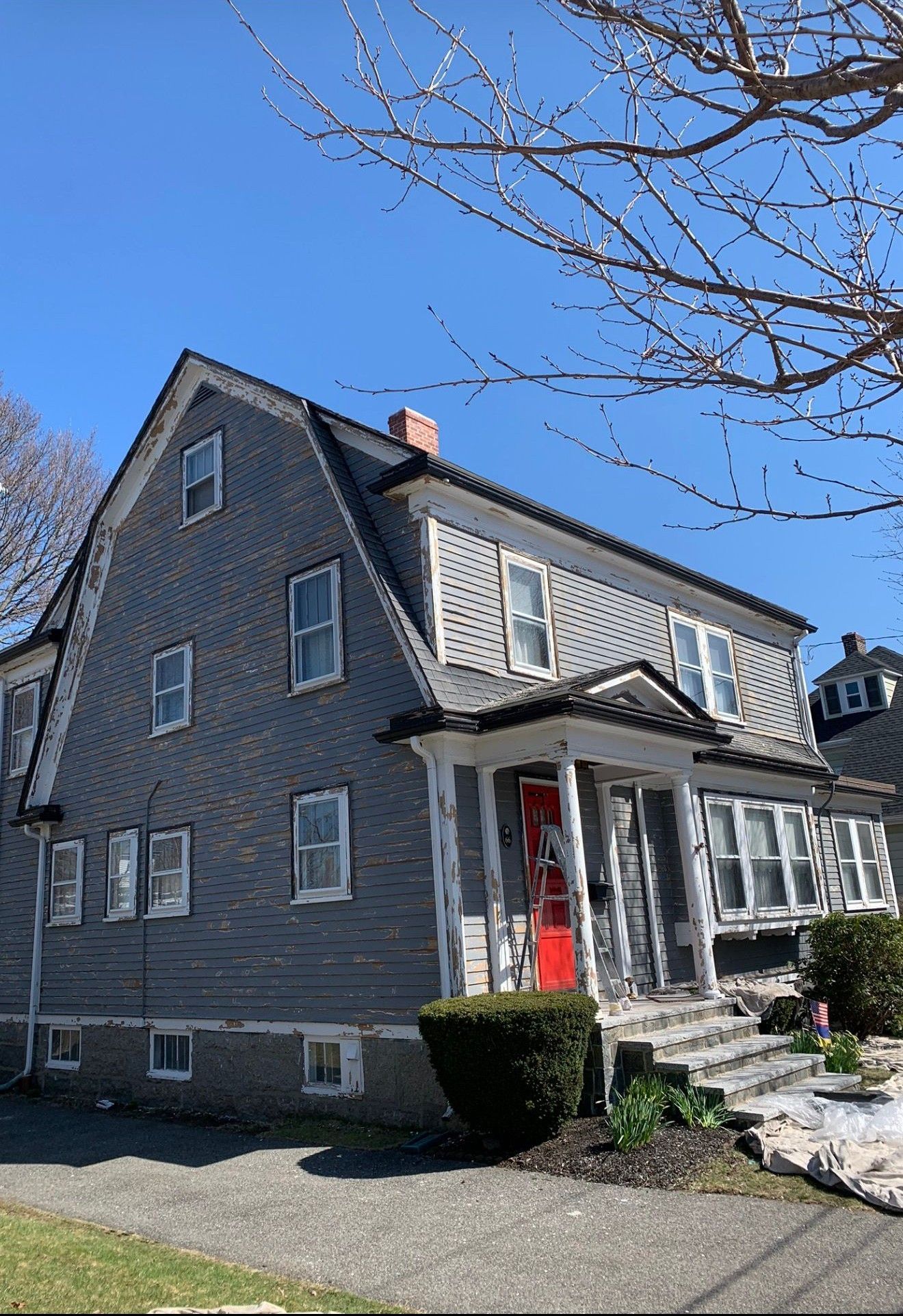 Gray house with red front door and small porch under a clear blue sky