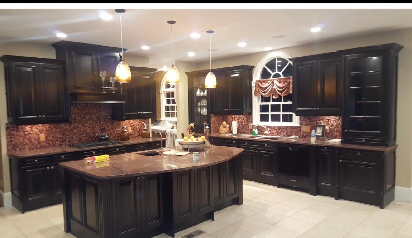 Spacious kitchen with dark wood cabinets, granite island, pendant lights, and tiled backsplash.